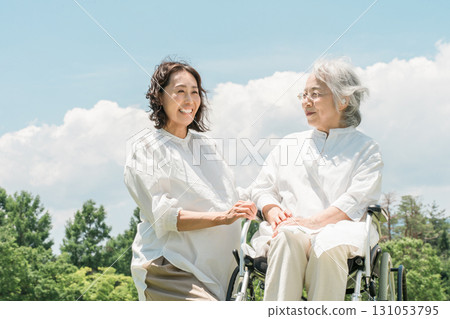 A senior woman in a wheelchair in a park and a woman assisting her (nursing care, parent and child, elderly care home) A senior woman in a wheelchair in a park and a woman assisting her (nursing care, parent and child, elderly care home) 131053795