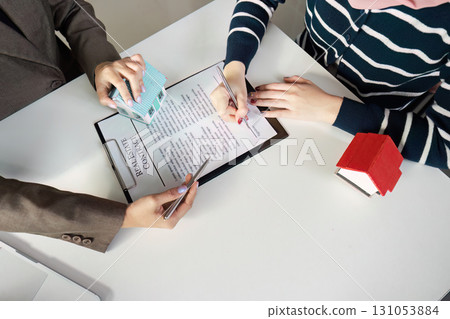 Real estate professional guiding client through contract signing with model houses on the table. 131053884