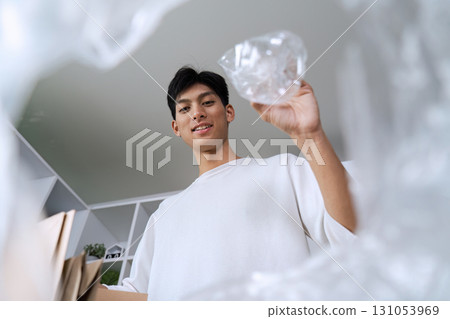 Young man smiling while holding recyclable plastic in eco-friendly workspace, promoting sustainability and recycling. Young man smiling while holding recyclable plastic in eco-friendly workspace, promoting sustainability and recycling. 131053969