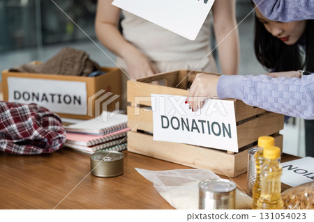 Individuals sorting items into donation boxes labeled for community support, organizing food and clothing contributions. 131054023