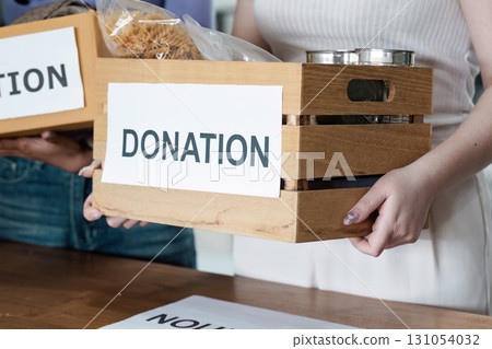 Woman holding a wooden donation box filled with food items, promoting community support and charitable efforts. 131054032