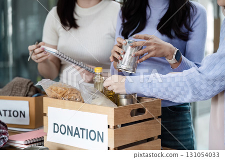 Group of women organizing food donations, including canned goods and pasta, for community support and charity efforts. 131054033