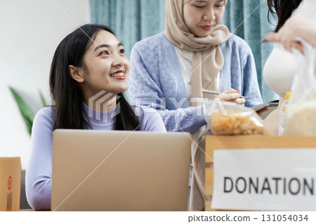 Diverse women collaborating on donation project, discussing contributions and community support in a modern workspace. 131054034