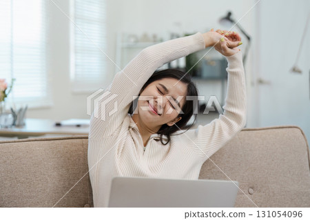 Diverse businesswoman stretching and relieving tension while working on her laptop at home, promoting wellness and self-care. Diverse businesswoman stretching and relieving tension while working on her laptop at home, promoting wellness and self-care. 131054096