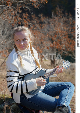 Blonde woman playing guitar ukulele outdoors in autumn forest. Concept of sound therapy, mental health and wellness rituals. Calmness tranquility audio-sensory practices. Aura farming Blonde woman playing guitar ukulele outdoors in autumn forest. Concept of sound therapy, mental health and wellness rituals. Calmness tranquility audio-sensory practices. Aura farming 131054122
