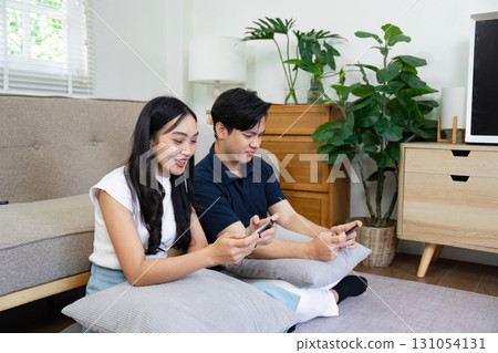 Couple enjoying a cozy lifestyle at home, playing games on their smartphones together. Couple enjoying a cozy lifestyle at home, playing games on their smartphones together. 131054131
