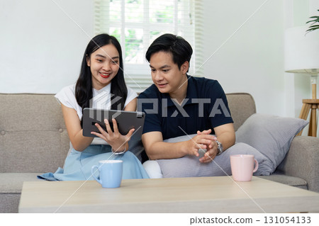 Couple enjoying a digital device together, sharing smiles and laughter in a comfortable living room. Couple enjoying a digital device together, sharing smiles and laughter in a comfortable living room. 131054133