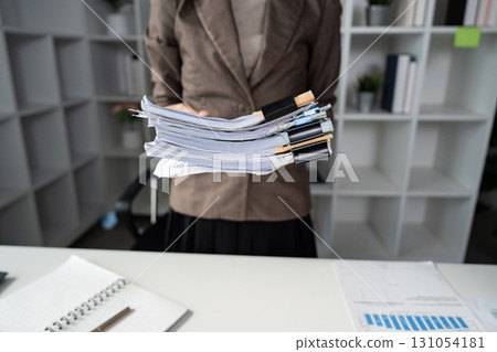 Organized businesswoman presenting a stack of financial documents in a modern office environment. 131054181