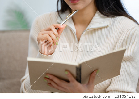 Woman brainstorming ideas in a cozy home office, jotting notes in a notebook with a pen. 131054182