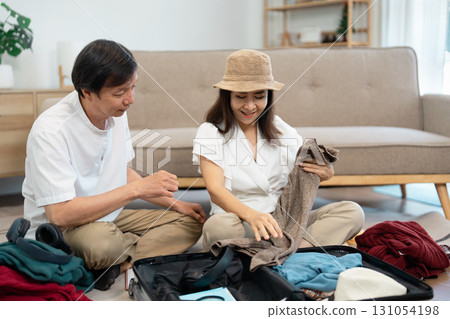Couple selecting outfits for their upcoming trip, sharing smiles and travel excitement in a relaxed home environment. 131054198