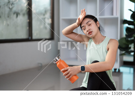 Tired woman wiping sweat after workout, promoting self-care and wellness at home. Tired woman wiping sweat after workout, promoting self-care and wellness at home. 131054209