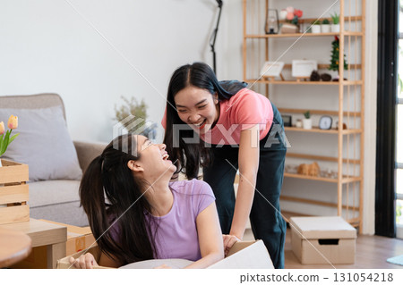 Diverse female couple laughing together while unpacking boxes in their new home. Diverse female couple laughing together while unpacking boxes in their new home. 131054218