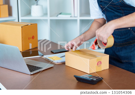 Diligent small business owner packing orders with tape in home office workspace 131054306