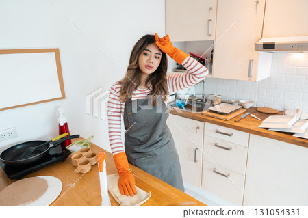 Woman in orange gloves wiping kitchen counter with a cloth 131054331