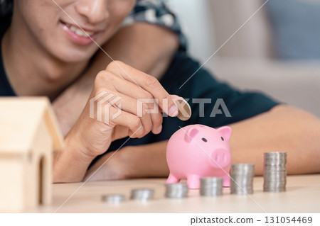 LGBTQ couple saving coins in a pink piggy bank at home, promoting financial literacy and savings LGBTQ couple saving coins in a pink piggy bank at home, promoting financial literacy and savings 131054469