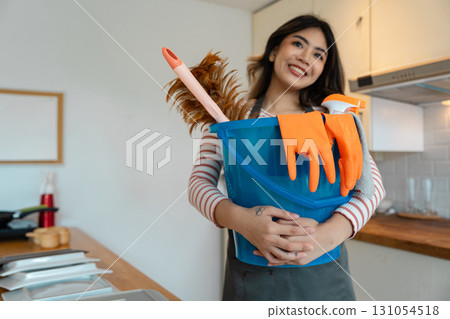 Smiling woman holding cleaning supplies in a blue bucket in the kitchen 131054518