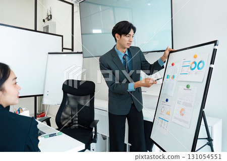 Dynamic Asian businessman presenting analytical data to a team during a meeting in a modern office. 131054551