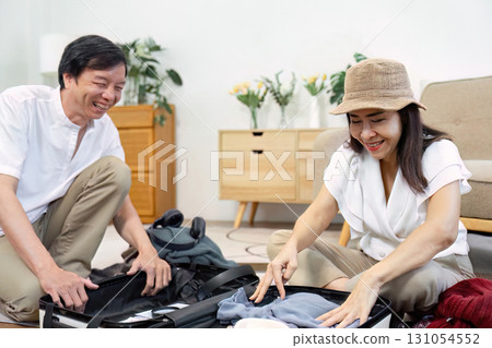 Senior couple joyfully packing a suitcase together while planning their travel adventure. Senior couple joyfully packing a suitcase together while planning their travel adventure. 131054552