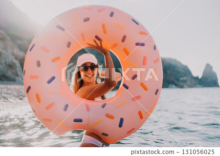 Woman, donut, sea, happy woman enjoys summer vacation in the ocean with an inflatable ring 131056025
