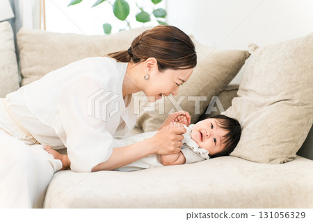 一位年輕的亞洲女性在沙發上安撫嬰兒（母親、育兒、養育） 131056329