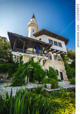 Balchik Palace in Bulgaria with stone walls, a minaret tower, EU and Bulgarian flags, and lush greenery by a pond with water lilies. Balchik Palace in Bulgaria with stone walls, a minaret tower, EU and Bulgarian flags, and lush greenery by a pond with water lilies. 131056972