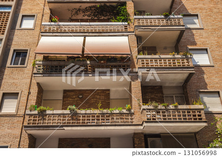 Facade of a residential building with balconies decorated with flower pots and plants in sunlight. 131056998