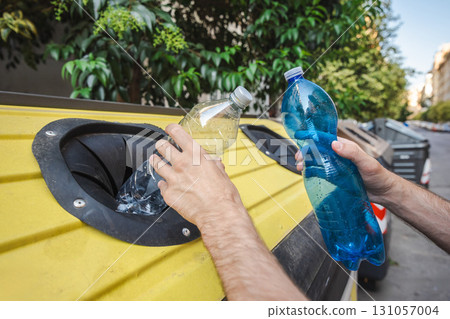 Man recycling plastic bottles into a yellow container on a street in Rome, Italy, emphasizing eco-friendly lifestyle and urban environmental responsibility. 131057004