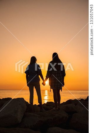 Silhouette of a middle-aged woman and a young woman holding hands on seaside rocks at sunrise 131057043