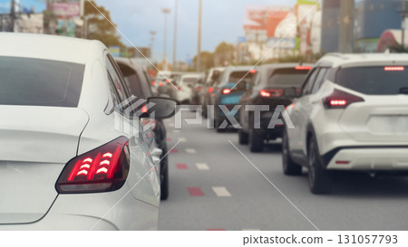 Rear side of white car and turn on brake light. Traffic is congested and there are long queues in the city. Blurred image of traffic jam with town under the blue sky. 131057793
