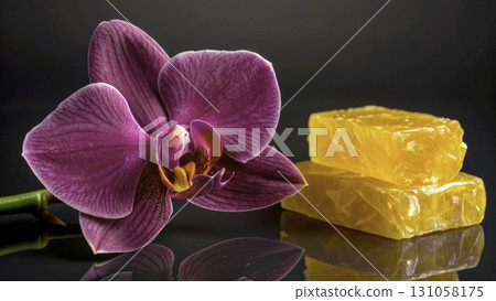 Bright purple orchid next to yellow soap bars on a reflective black surface in a serene setting 131058175