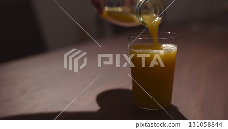 man pour organic orange juice from glass bottle into tumbler glass on walnut table man pour organic orange juice from glass bottle into tumbler glass on walnut table 131058844