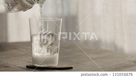 Pour tonic over clear ice cube in tumbler glass on black oak table Pour tonic over clear ice cube in tumbler glass on black oak table 131058876