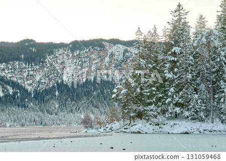 A picturesque evening landscape view of the frozen Eibsee lake at the foot of the Zugspitze mountain, showcasing a serene winter scene with snow-covered pine trees, a snowy forest. Twilight Alpine A picturesque evening landscape view of the frozen Eibsee lake at the foot of the Zugspitze mountain, showcasing a serene winter scene with snow-covered pine trees, a snowy forest. Twilight Alpine 131059468