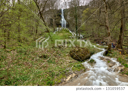 Cascading Waterfall in Lush Forest with Moss-Covered Rocks, Fast-Moving Stream, Wooden Bridge, Serene and Picturesque Atmosphere. 131059537