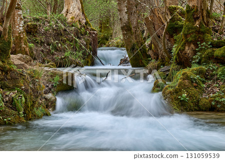Lively Rushing Stream in Verdant Natural Setting, Vibrant Turquoise Water, Lush Greenery, Dynamic Texture, Rugged Rocky Banks, Early Spring Atmosphere. 131059539