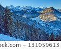 Snowy Mountain Landscape with Iconic Castle Overlooking Serene Lake and Alpine Peaks in Ethereal Winter Wonderland Bathed in Soft Dawn Light 131059613