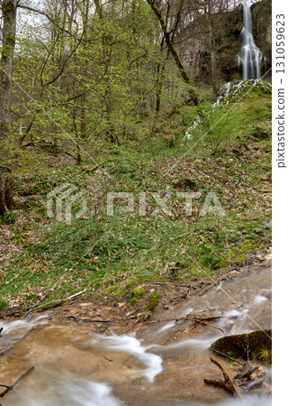 Serene Forest Waterfall with Wooden Bridge and Observers in Lush Greenery. Serene Forest Waterfall with Wooden Bridge and Observers in Lush Greenery. 131059623
