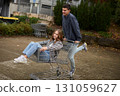 Happy young couple having fun with a shopping cart outdoors in autumn park, wearing stylish casual outfits with denim and flannel, laughing and enjoying the moment. 131059627