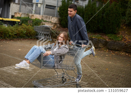 Happy young couple having fun with a shopping cart outdoors in autumn park, wearing stylish casual outfits with denim and flannel, laughing and enjoying the moment. Happy young couple having fun with a shopping cart outdoors in autumn park, wearing stylish casual outfits with denim and flannel, laughing and enjoying the moment. 131059627