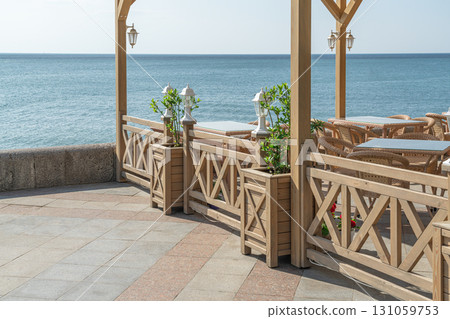 Coastal Dining Area With Wooden Barriers and Ocean View in Bright Sunlight Coastal Dining Area With Wooden Barriers and Ocean View in Bright Sunlight 131059753