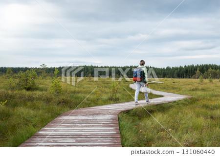Woman with basket of mushrooms, returning from forest along wooden path through peat bog in autumn 131060440
