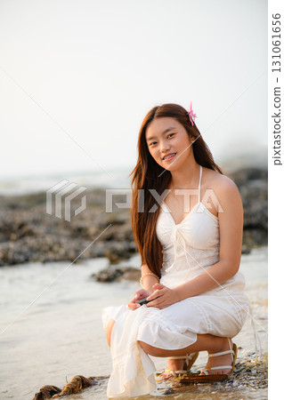A woman in a white dress is enjoying her vacation on the beach with a retro camera in hand. 131061656