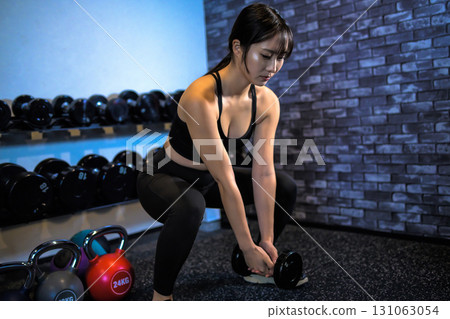 一位女士正在用啞鈴深蹲訓練臀部。一位酷酷的女士正在健身房鍛鍊。臀部訓練。肌肉訓練女孩。 131063054