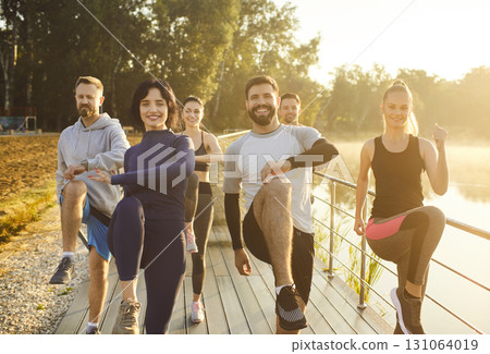 Team of athlets doing exercises outdoors, raising legs, demonstrating strething abilities 131064019