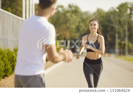 Young athletic girl running to the finish to a man supporting her standing in city park outdoors. 131064029