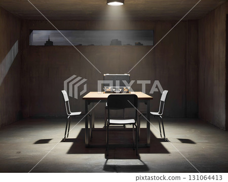 The interior of an empty interrogation room. A simple metal table and two chairs stand in the center. The walls have a gray, concrete texture, and a blurred cityscape is visible through a small window 131064413