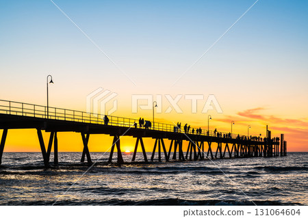 Stunning sunset at Glenelg Beach jetty, with silhouettes of people 131064604