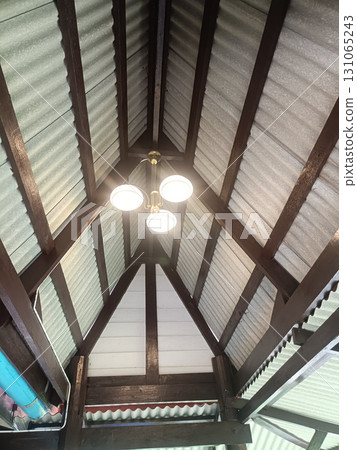 Image shows high ceiling with chandelier light fixture hanging from center, surrounded by wooden beams and corrugated metal roofing panels Image shows high ceiling with chandelier light fixture hanging from center, surrounded by wooden beams and corrugated metal roofing panels 131065243