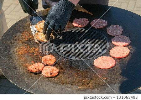 Chef man cooking burger patties on grill turning with spatula in street cafe. 131065488