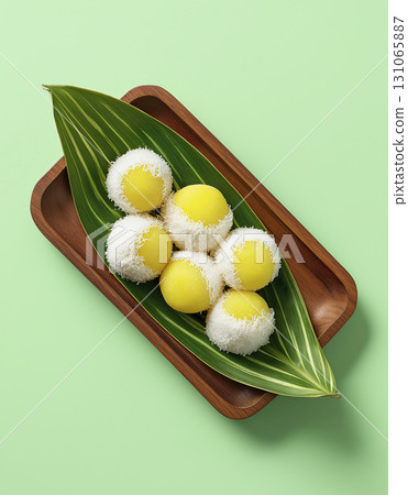 Delicious yellow mochi balls with white coconut flakes green leaf wooden tray fresh and appealing dessert vibrant colors tropical theme sweet 131065887